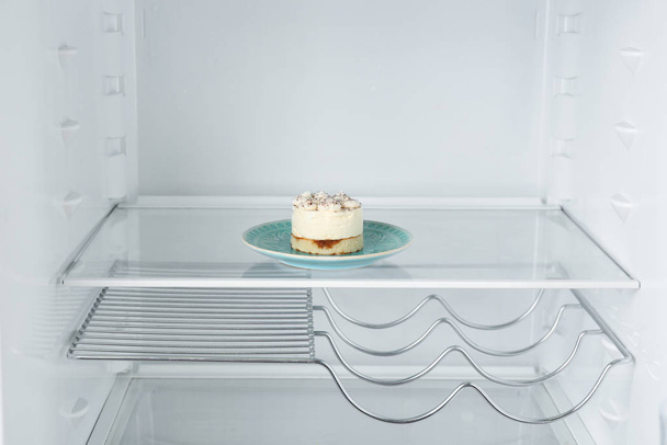 Тарелка с вкусным десертом на пустой полке в холодильнике
 - Фото, изображение