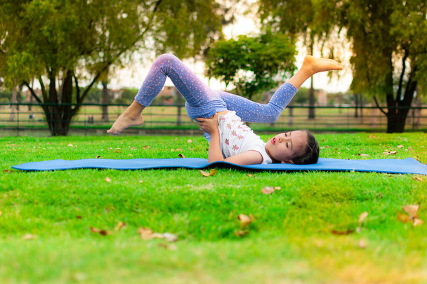 beautiful girl practices yoga at sunrise on the grass in a park - Фото, изображение