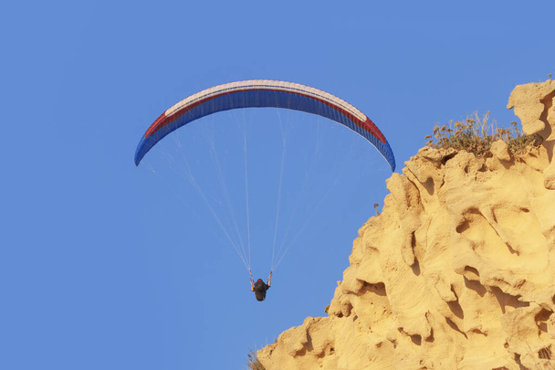 Paraglider sininen taivas ja keltainen hiekkakivi kallio
 - Valokuva, kuva