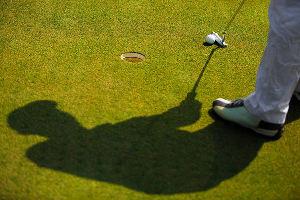 Тень гольфиста, который собирается забить мяч для гольфа
 - Фото, изображение