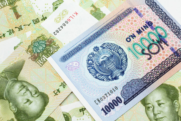 Зображення банкноти номіналом у десять тисяч узбецьких сомів на тлі зелених, китайських юаней на макрофонді. - Фото, зображення