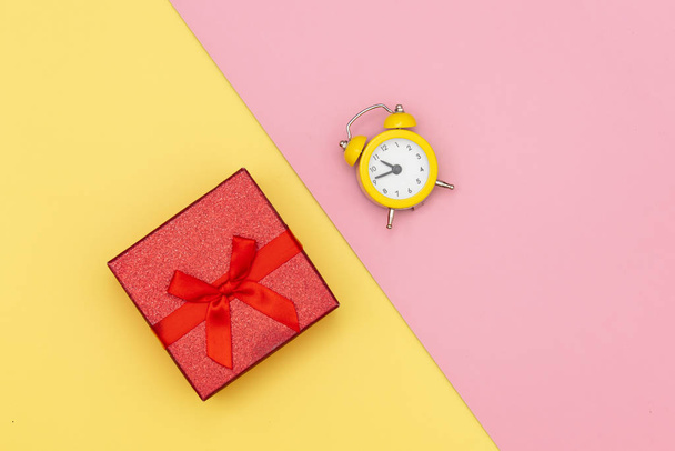 Little gift box and alarm clock on pink and yellow backgrounds. Above view - Valokuva, kuva