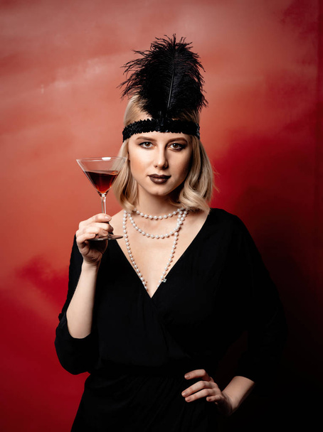 Beautiful blonde woman in twenties years clothes with cocktail on dark background - Valokuva, kuva