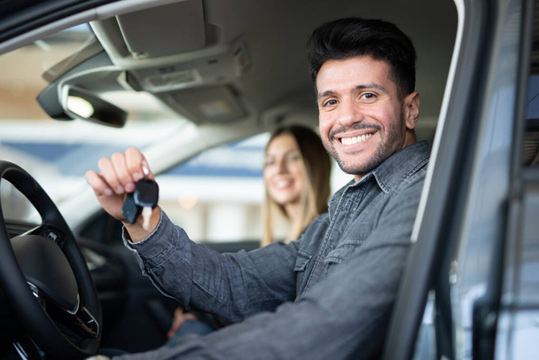 Young happy man showing the key of his new car in a car dealer saloon - Photo, Image