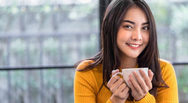 Asiatique jeune femme tenant une tasse de café dans un café moderne ou un espace de coworking à côté miroir de fenêtre, Lifestyle et loisirs avec hobby et concept d'entrepreneur, bannière ou échelle de couverture web
 - Photo, image