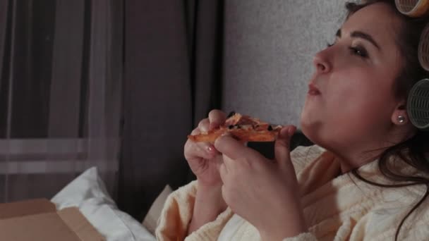 Läski tyttö syö pizzaa sängyssä. Liikalihavuus, modernin ravitsemuksen ongelmat, pikaruoka, ruokavalio, syödä yöllä. Ylipaino-ongelmat
. - Materiaali, video