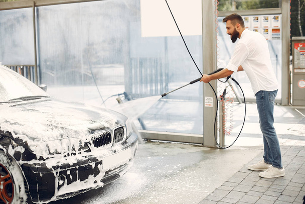Handsomen man in a white shirt washing his car - 写真・画像