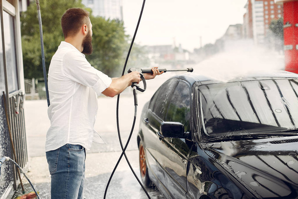 Handsomen man in a white shirt washing his car - Фото, изображение