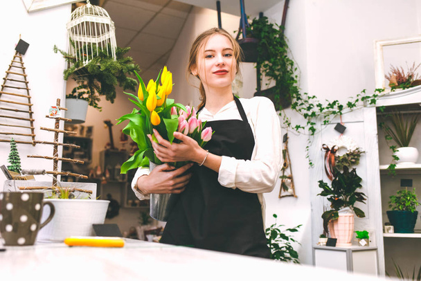 Portret sprzedawcy kwiatów z tulipanami w rękach. Młoda kwiaciarnia pracuje w kwiaciarni - Zdjęcie, obraz