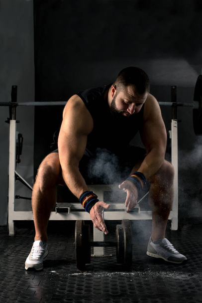 Powerlifter with strong arms is preparing a weightlifting. Muscular man training in the gym. Healthy lifestyle concept. - 写真・画像