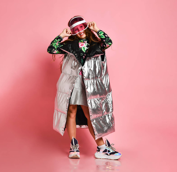 Young happy plus size girl in floral printed casual clothing, metallic coat, cap standingand holding cap mixed with sunglasses - 写真・画像
