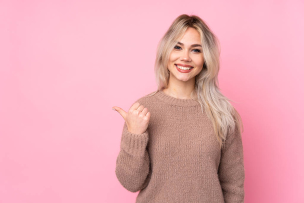 Teenager blondes Mädchen trägt einen Pullover über isoliertem rosa Hintergrund, der zur Seite zeigt, um ein Produkt zu präsentieren - Foto, Bild