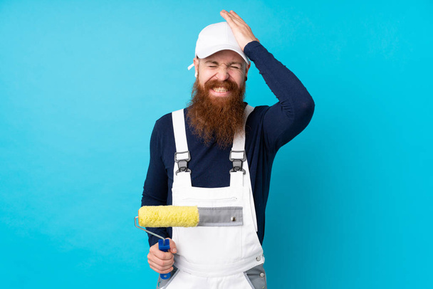 Homem pintor com barba longa sobre fundo azul isolado com dúvidas com expressão facial confusa
 - Foto, Imagem