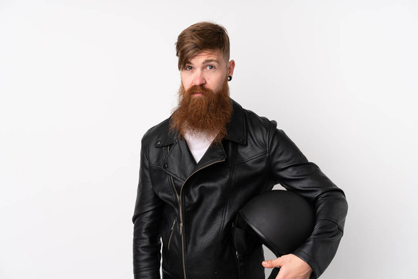 Redhead man with long beard holding a motorcycle helmet over isolated white background sad - Photo, Image