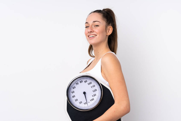 Young brunette woman over isolated white background with weighing machine - Φωτογραφία, εικόνα