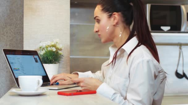 Beautiful latino woman working on a laptop and talking on the phone at work. Work at home, freelance, modern technology. Internet Serving - Imágenes, Vídeo