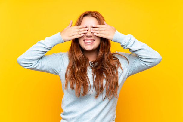 tiener roodharige meisje over geïsoleerde gele achtergrond bedekken ogen door handen - Foto, afbeelding