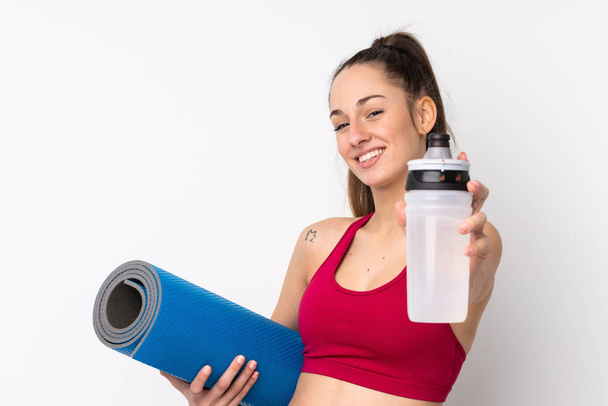 Young sport brunette woman over isolated white background with sports water bottle and with a mat - Foto, Imagen