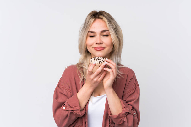 Teenager blonde girl over isolated white background holding a donut - Fotó, kép