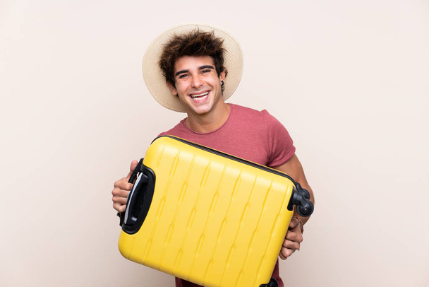 Young caucasian man over isolated background in vacation with suitcase and passport - 写真・画像