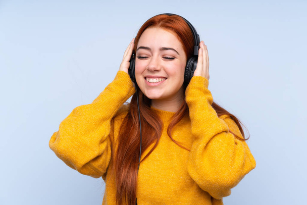 Piros hajú tinédzser lány elszigetelt kék háttér hallgat zenét - Fotó, kép