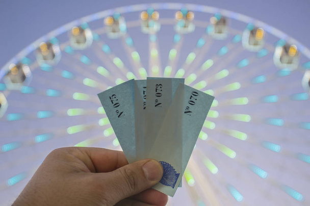 Рука с кулаком билетов на гигантский аттракцион колеса обозрения
 - Фото, изображение