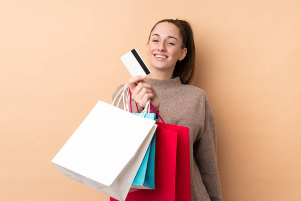 Молодая брюнетка на изолированном фоне держит сумки с покупками и кредитку
 - Фото, изображение