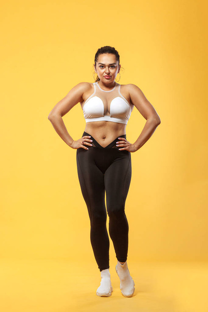 Size plus woman sporty fit woman in sportswear, athlete makes fitness exercising on yellow background. Motivation for fat people. - Fotografie, Obrázek