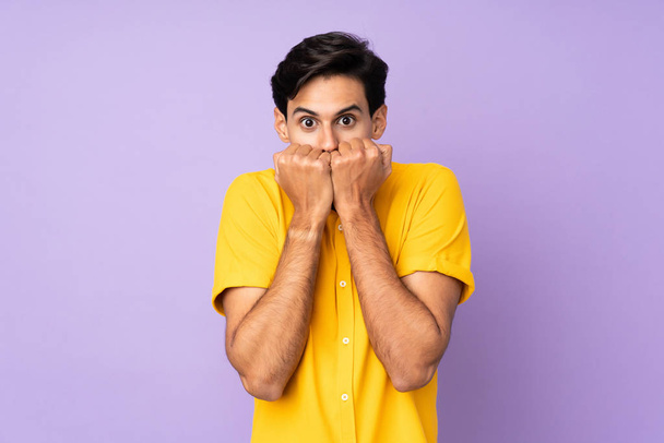 Людина над ізольованим фіолетовим тлом нервує і боїться прикладати руки до рота
 - Фото, зображення