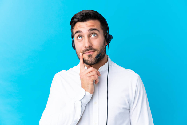 Telemarketer man working with a headset over isolated blue background thinking an idea - Photo, Image