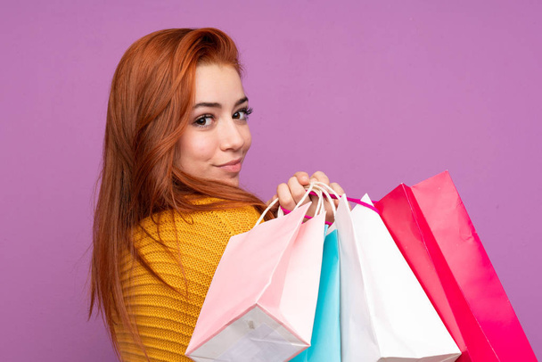 Ruiva adolescente sobre isolado roxo fundo segurando sacos de compras
 - Foto, Imagem