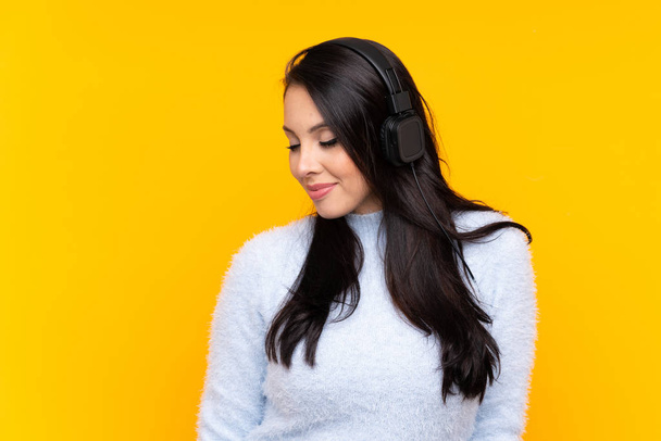 Giovane ragazza colombiana su sfondo giallo isolato ascoltare musica - Foto, immagini