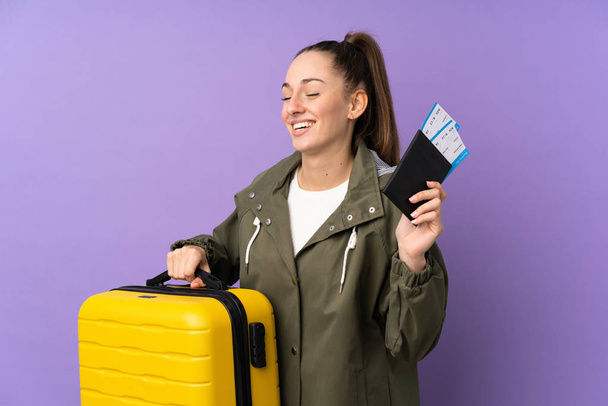 Young brunette woman over isolated purple background in vacation with suitcase and passport - Фото, изображение