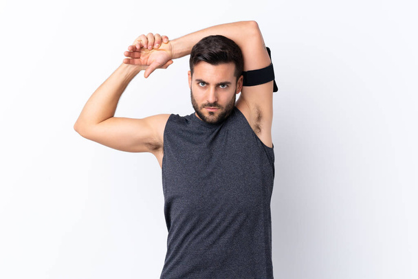 Jonge sport knappe man met baard over geïsoleerde witte achtergrond stretching arm - Foto, afbeelding