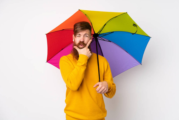 Uomo dai capelli rossi con lunga barba che tiene un ombrello su uno sfondo bianco isolato pensando a un'idea - Foto, immagini