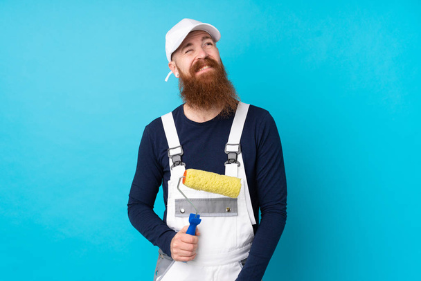 Художник с длинной бородой на изолированном синем фоне смеется и смотрит вверх
 - Фото, изображение