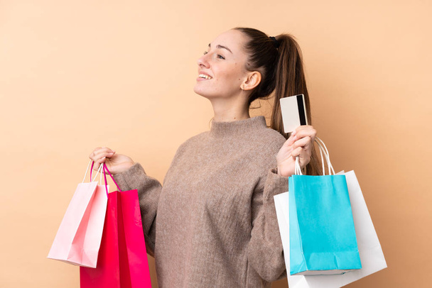 jonge brunette vrouw over geïsoleerde achtergrond holding boodschappentassen en een creditcard - Foto, afbeelding