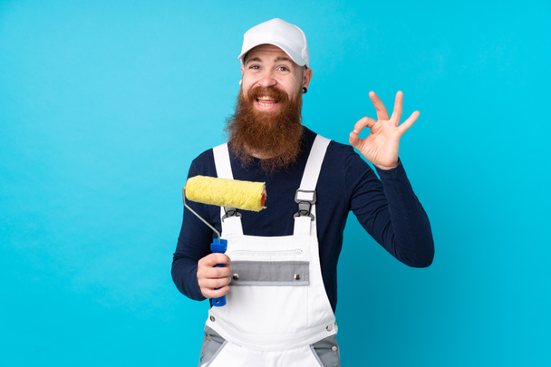 Художник с длинной бородой на изолированном синем фоне показывает знак ОК с пальцами - Фото, изображение