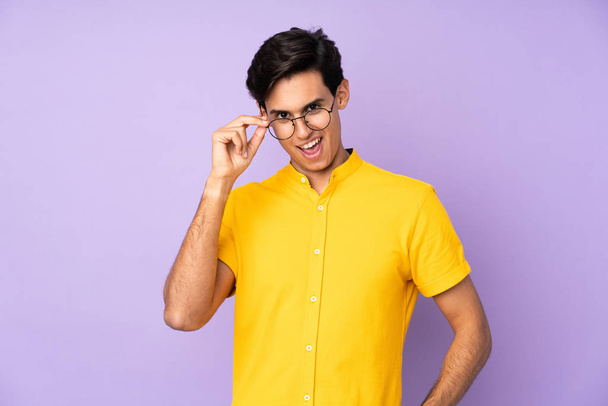Mann über isoliertem lila Hintergrund mit Brille und glücklich - Foto, Bild