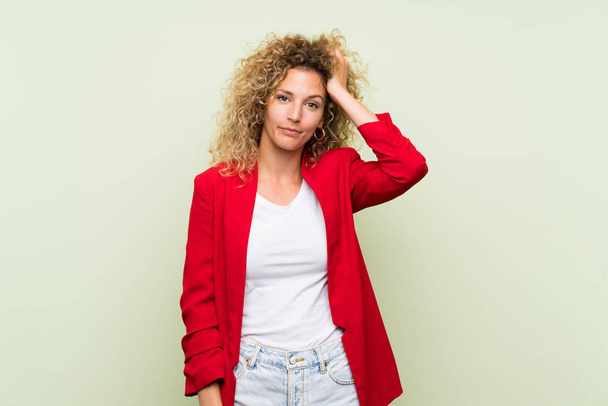 Young blonde woman with curly hair over isolated green background with an expression of frustration and not understanding - Photo, image