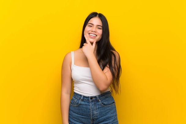 junge Teenager asiatische Mädchen über isolierte gelbe Hintergrund lächelnd - Foto, Bild