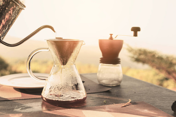Käsi tippuu kahvi keitto kaada kahvia kuumalla vedellä kaadetaan vedenkeitin vuoristomaisemat ja luonnollinen vihreä näkymä tunne chill ja rentoutua luonnossa - Valokuva, kuva
