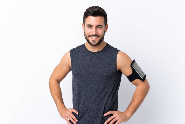 Young sport handsome man with beard over isolated white background posing with arms at hip and smiling - Photo, Image