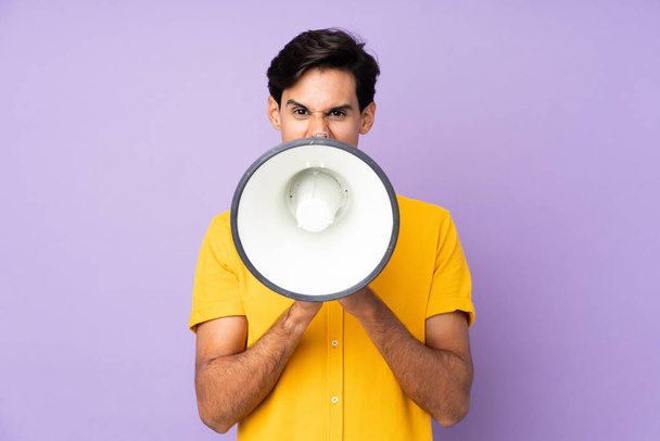 Man over isolated purple background shouting through a megaphone - Zdjęcie, obraz