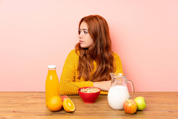 Teenager redhead girl having breakfast in a table looking side - Фото, зображення