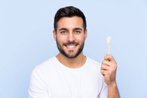 Young handsome man with beard brushing his teeth over isolated background smiling a lot - Foto, Imagem