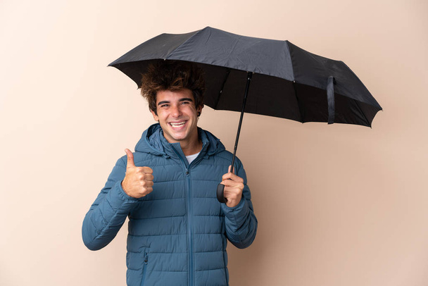 Mann hält Regenschirm mit erhobenem Daumen über isoliertem Hintergrund, weil etwas Gutes passiert ist - Foto, Bild