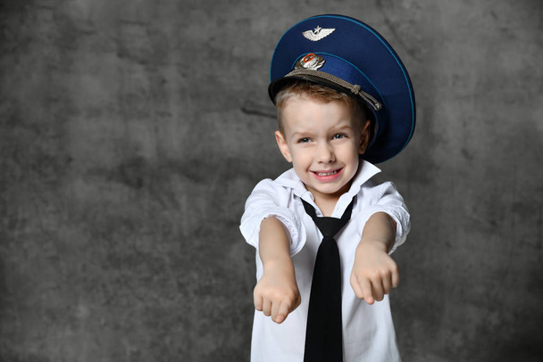 Niño sonriente en camisa blanca, jeans, corbata y gorra de policía de pie y jugando en el policía sobre fondo gris
 - Foto, imagen