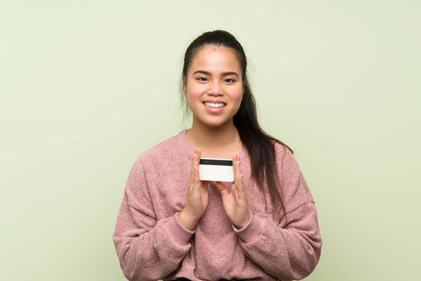 Молодий підліток Азіатська дівчина над ізольованою зелений фон проведення кредитної картки - Фото, зображення
