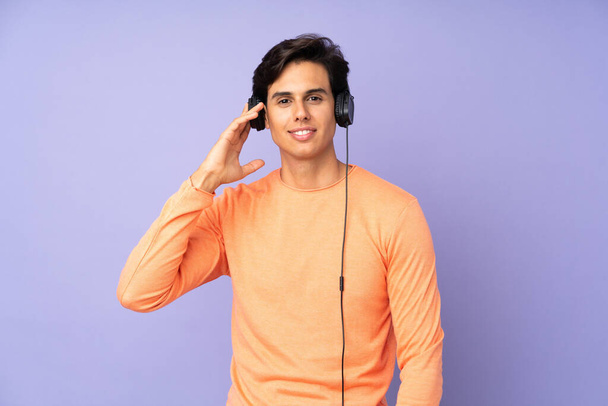 Man over geïsoleerde paarse achtergrond luisteren muziek - Foto, afbeelding